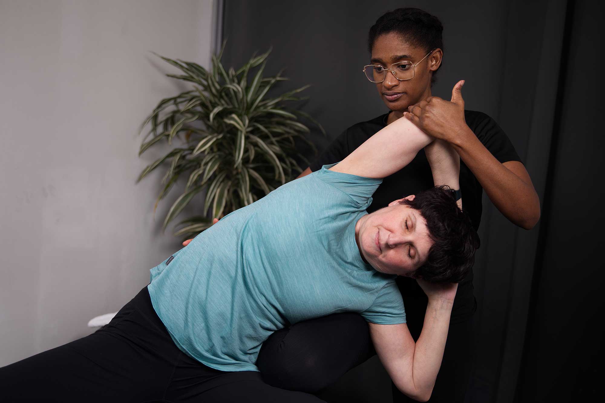 A professional stretch therapist guiding a client through a deep side and lat stretch at Vive Fitness in London.