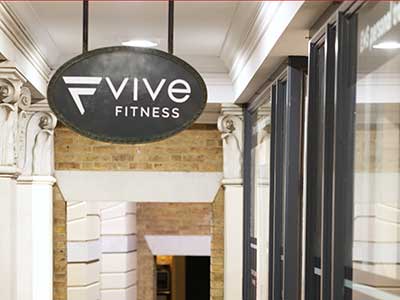 The Vive Fitness branded hanging sign outside the Richmond studio, set against traditional architectural pillars.