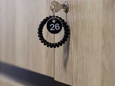 A close-up of a secure wooden locker with a key and numbered wristband tag at the Vive Fitness studio.