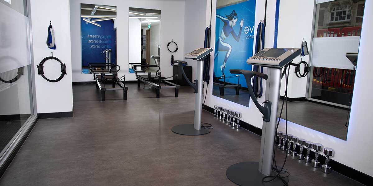 A wide interior view of the modern Vive Fitness Westminster studio, featuring EMS training consoles, Pilates reformers, and professional strength equipment.
